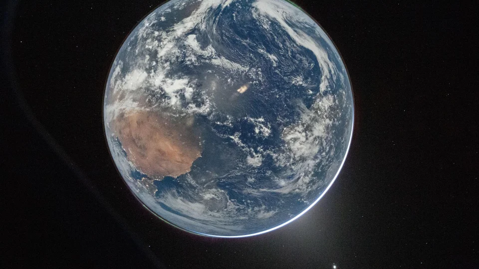 Earth's moonlit nightside as seen from Artemis II, with green auroral bands at both poles, city lights across Africa and South America, and stars in the background (NASA / Reid Wiseman)