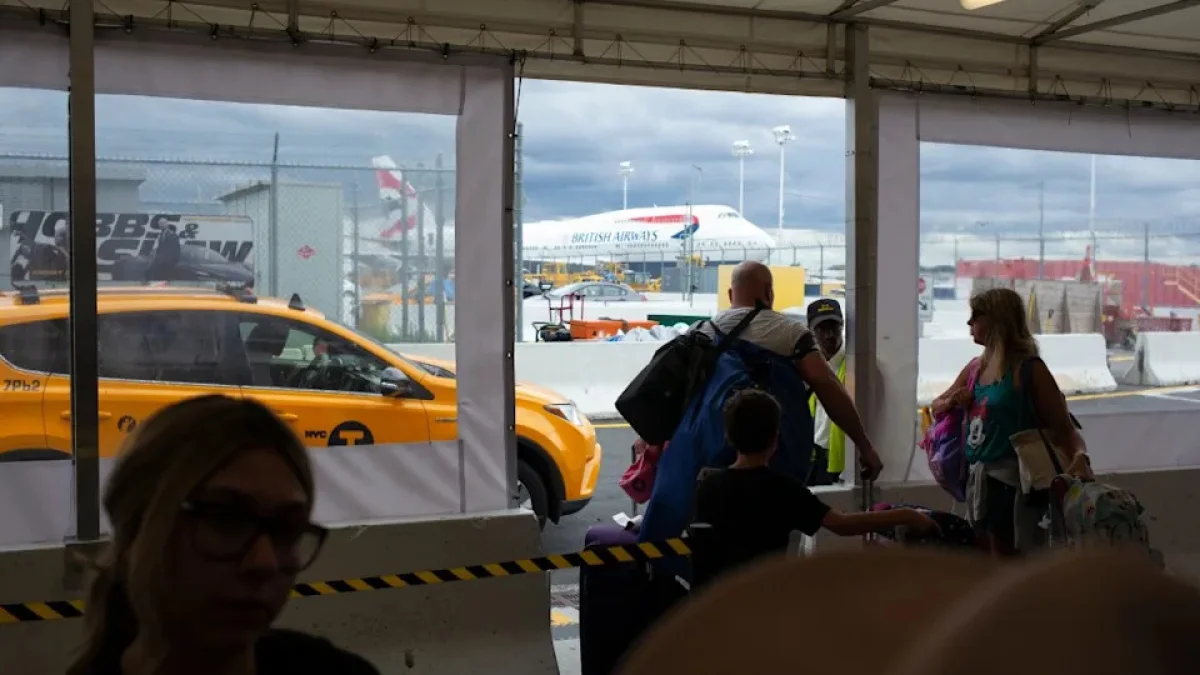 Travelers with luggage at a New York City airport taxi queue near a yellow cab and British Airways aircraft on the tarmac