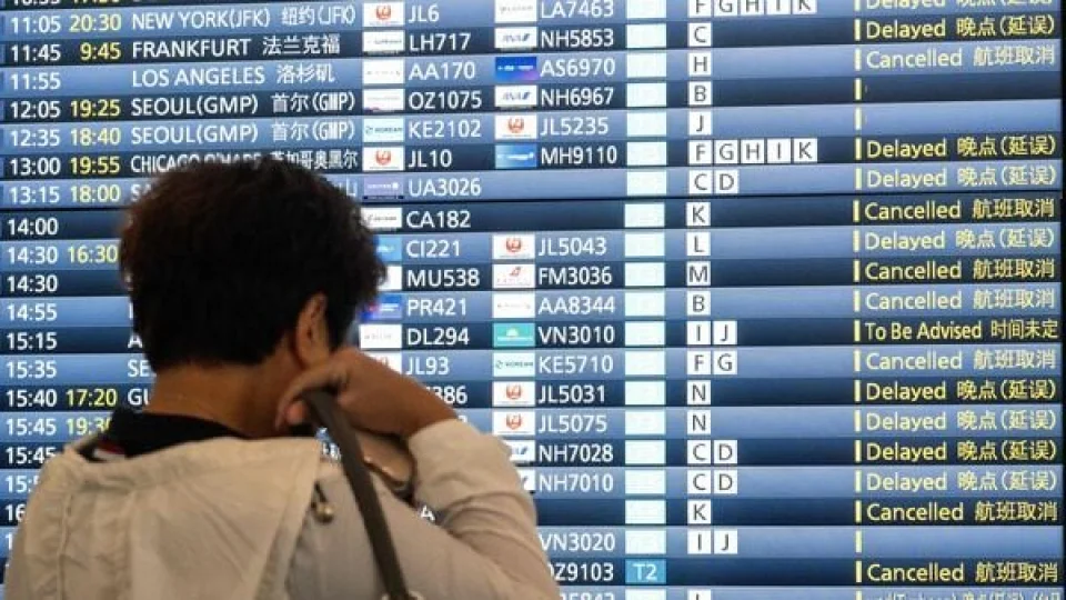 Traveler at an airport departure board showing delayed and cancelled flights including Chicago O'Hare during severe weather disruption